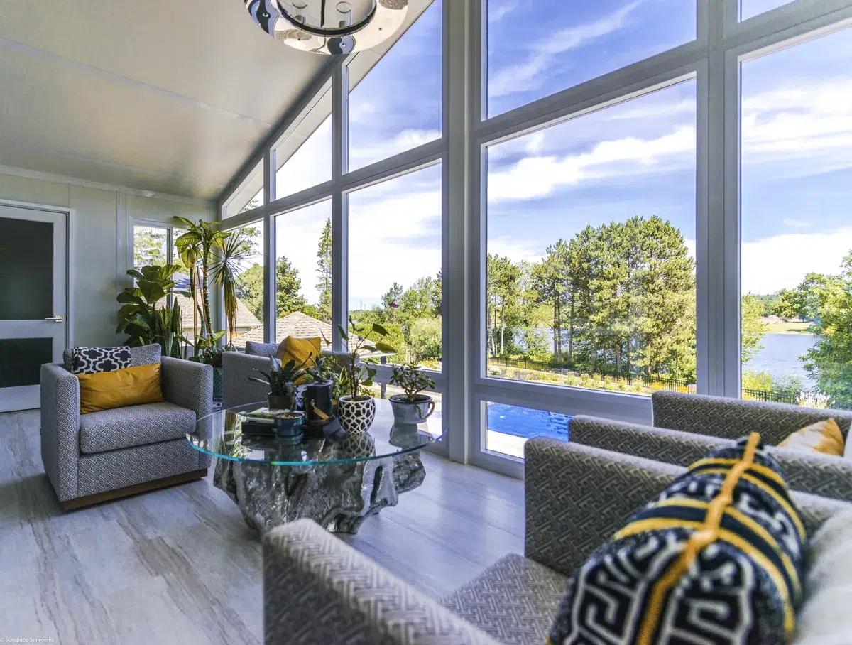 Comfortable seating area in a bright sunroom with large windows overlooking a lake.