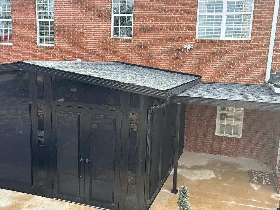 A black Sunspace sunroom with a shingled roof addition on a brick house patio.