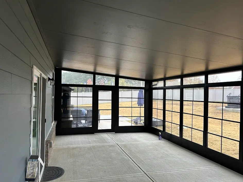 An empty modern Sunspace sunroom patio enclosure with black frames overlooking a backyard.