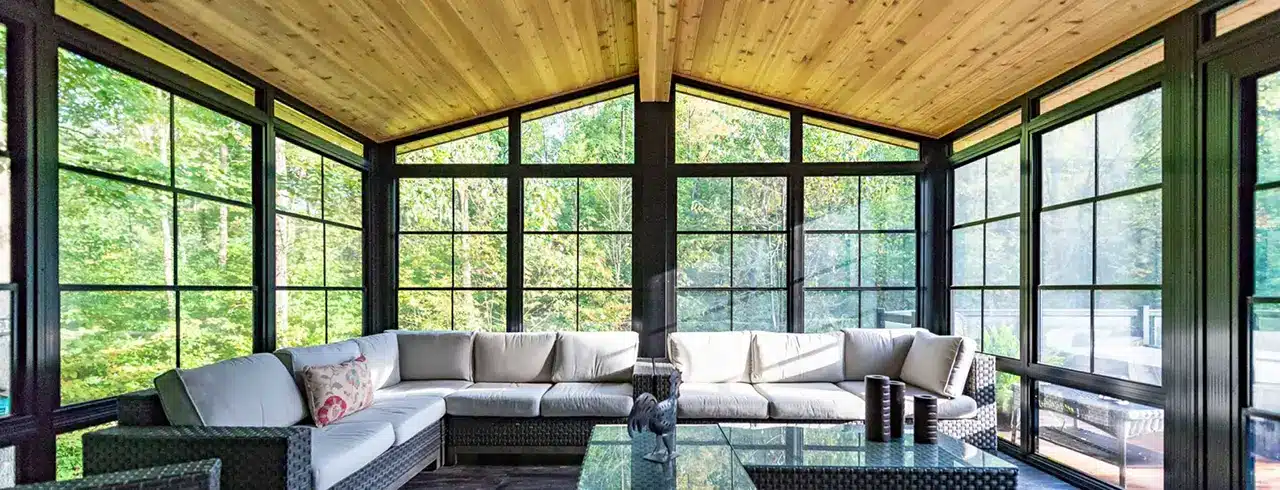 Stunning vaulted wood ceiling sunroom featuring dark frame WeatherMaster windows and large sectional sofa.
