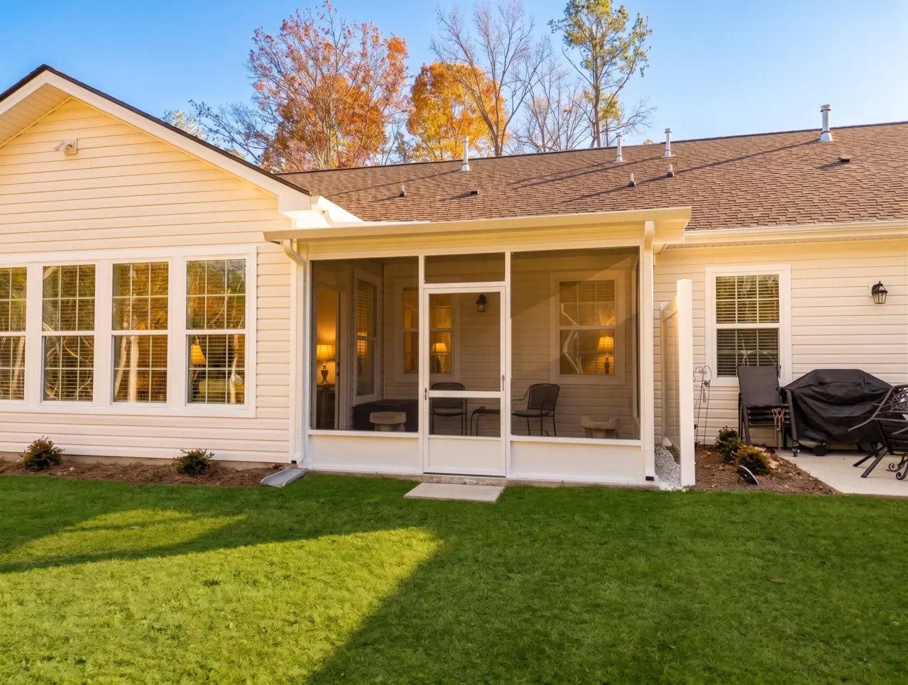 A white-framed screen room attached to the back of a residential house, overlooking a lush green lawn.