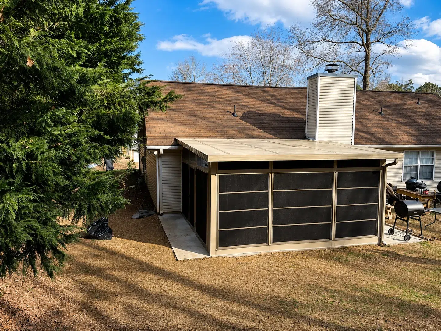 Backyard view of an attached screen room enclosure with screened panels, beige roof, and patio space for a Myrtle Beach home upgrade.