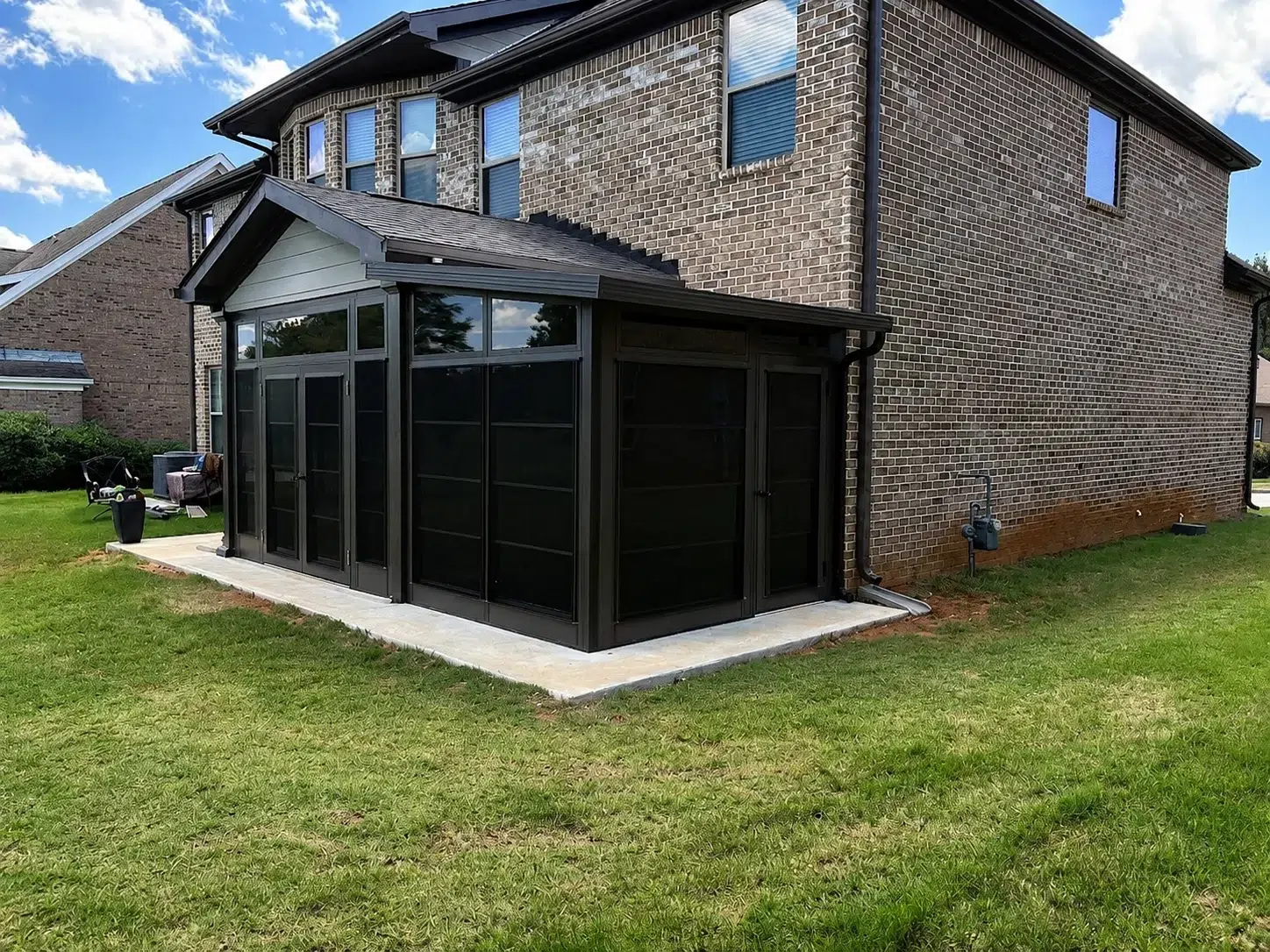 Black screen room addition attached to a brick home, creating a covered backyard patio enclosure for comfortable outdoor living.