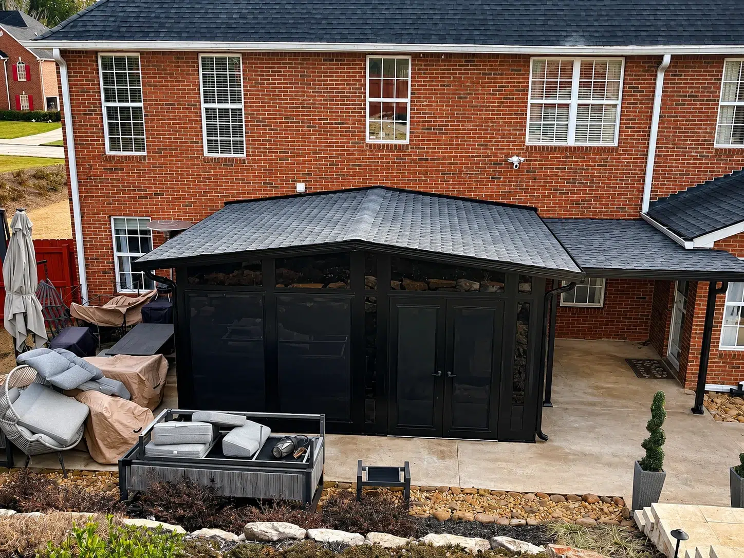 Black screen room enclosure attached to a red brick home with dark roof, double doors, patio furniture, and backyard space in Myrtle Beach.