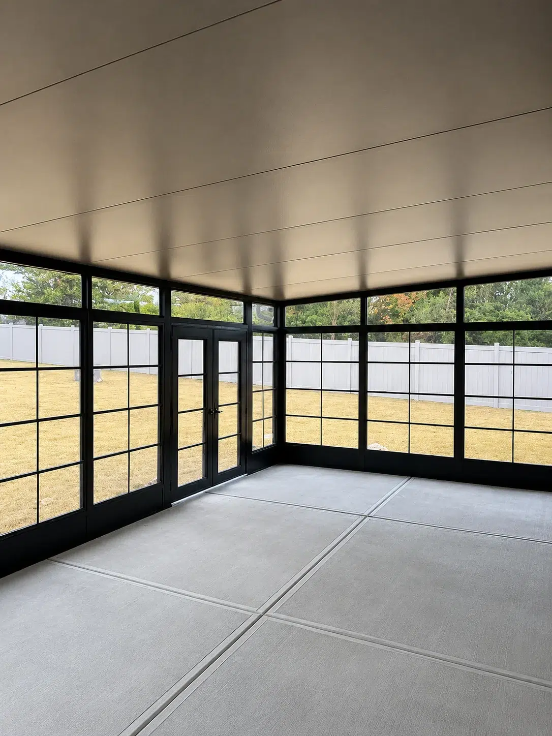 Interior black screen room with large screened panels, double doors, concrete flooring, and backyard views for protected outdoor living.