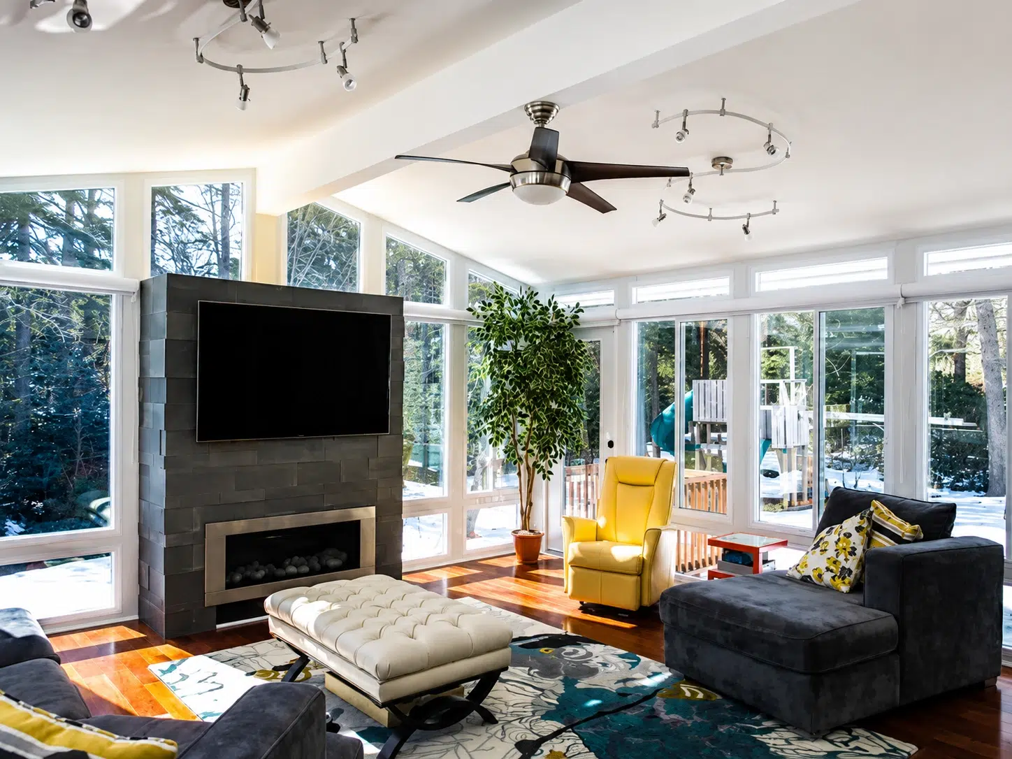 A modern sunroom living area with floor-to-ceiling windows, natural light, fireplace, and comfortable seating