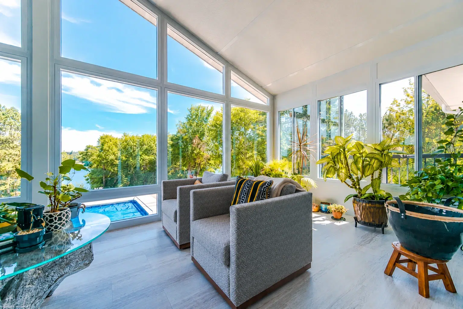 A bright modern sunroom with large glass windows, indoor plants, comfortable seating, and a beautiful outdoor garden view.