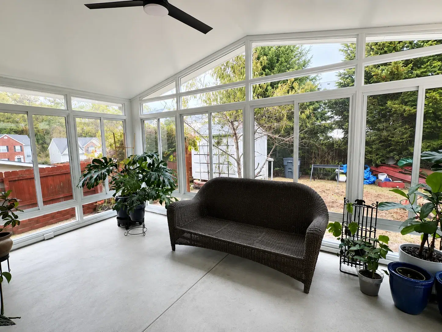 Bright white sunroom interior with large windows, ceiling fan, wicker sofa, indoor plants, and backyard views for Myrtle Beach living.