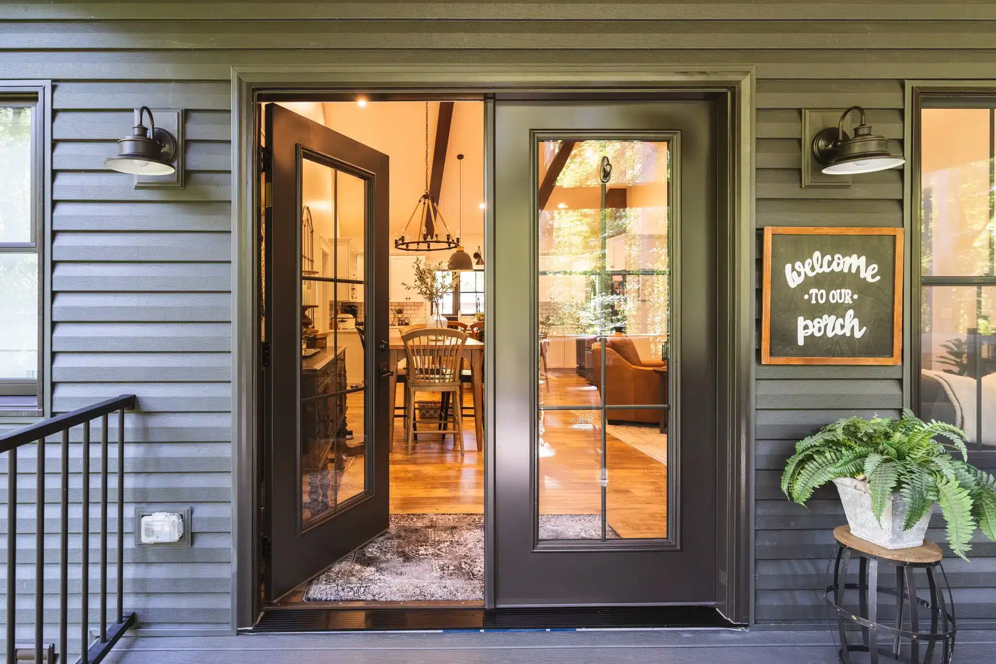 Exterior view of a dark-framed Sunspace WeatherMaster door featuring glass panels with grid detailing, installed as a stylish entryway to a warm, inviting porch setting.