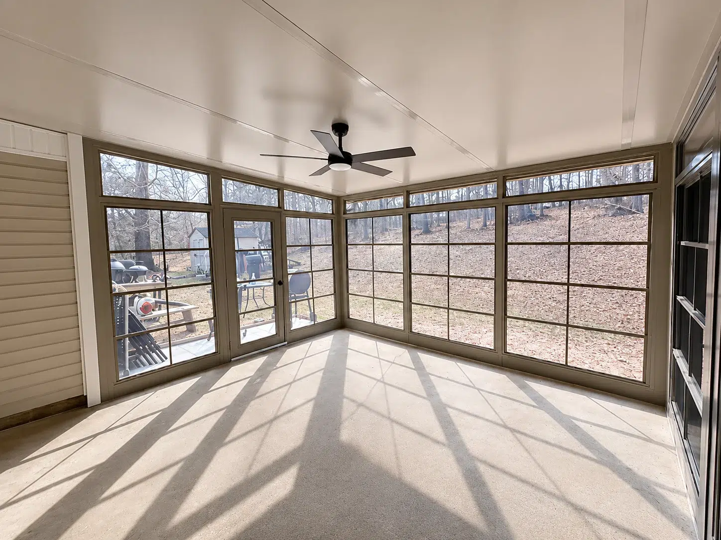 Tan screen room interior with large screened windows, ceiling fan, concrete floor, and wooded backyard views for Myrtle Beach outdoor living.
