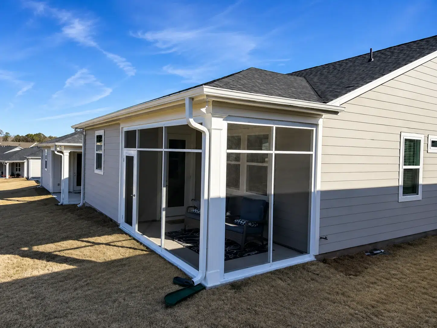 White frame screen room enclosure attached to a residential home with screened walls, glass door, and backyard view.