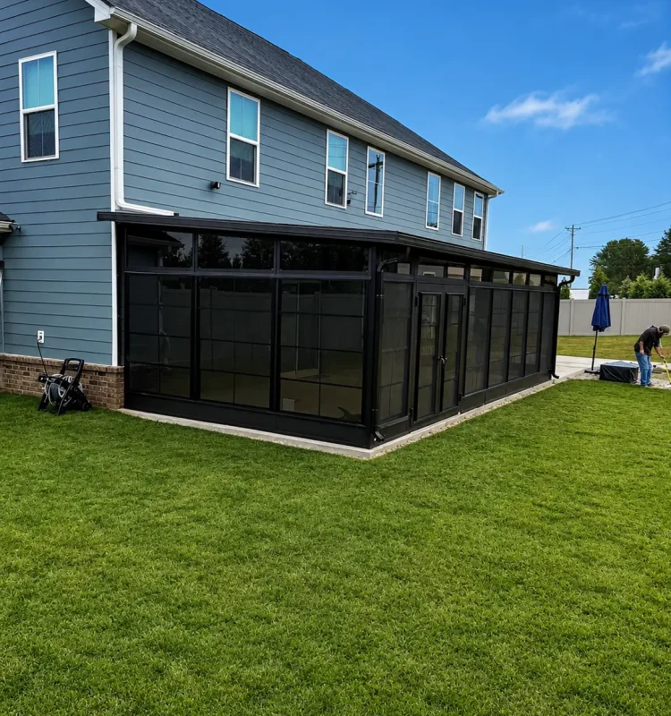 Exterior view of a modern black-framed sunroom addition attached to a blue home.